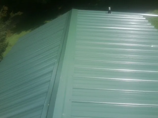New green metal panels meeting at the ridge of a roof — Flat Roof Repair work by our crew in Saltillo
