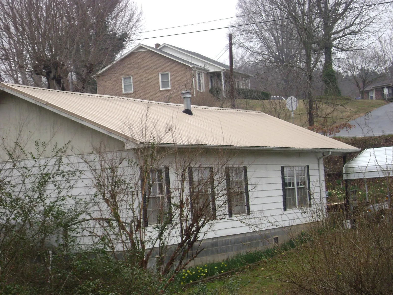 Tan metal roof on a white sided house set into a hillside — Commercial Roofing by Roofing Brothers in Saltillo